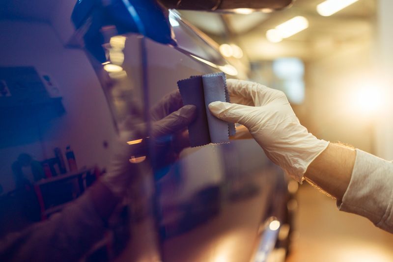 Person wearing gloves closely applying a ceramic coating to the shining blue paint surface of a car, enhancing its finish