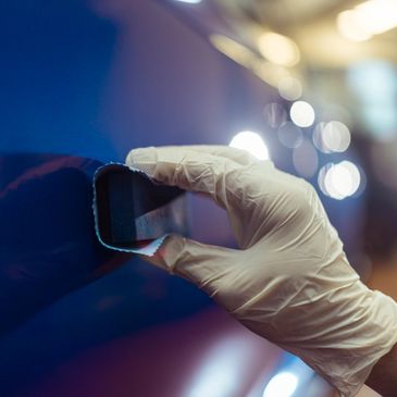 Gloved hand cleaning a smooth surface with a cloth.