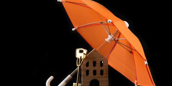 Orange umbrella protecting a small wooden house model.