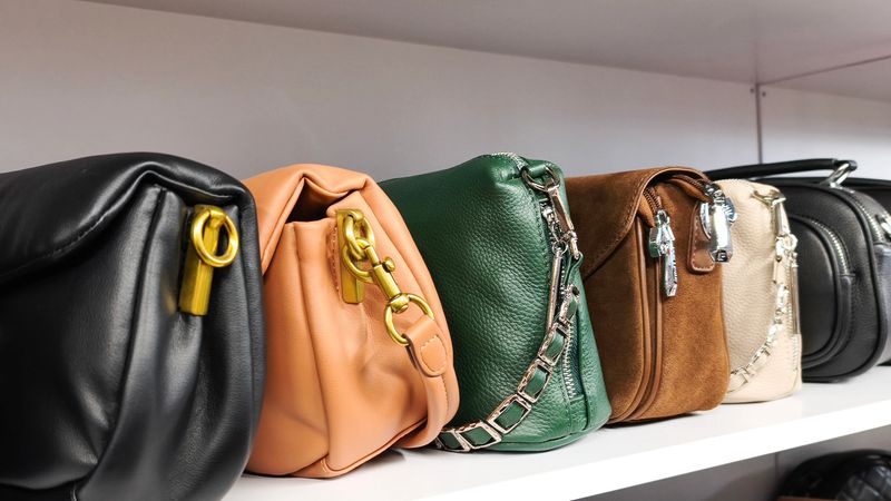 Leather handbags in black, peach, green, brown, and beige colors neatly arranged on store shelf, fashion retail concept, shopping and accessory display, stylish and organized interior