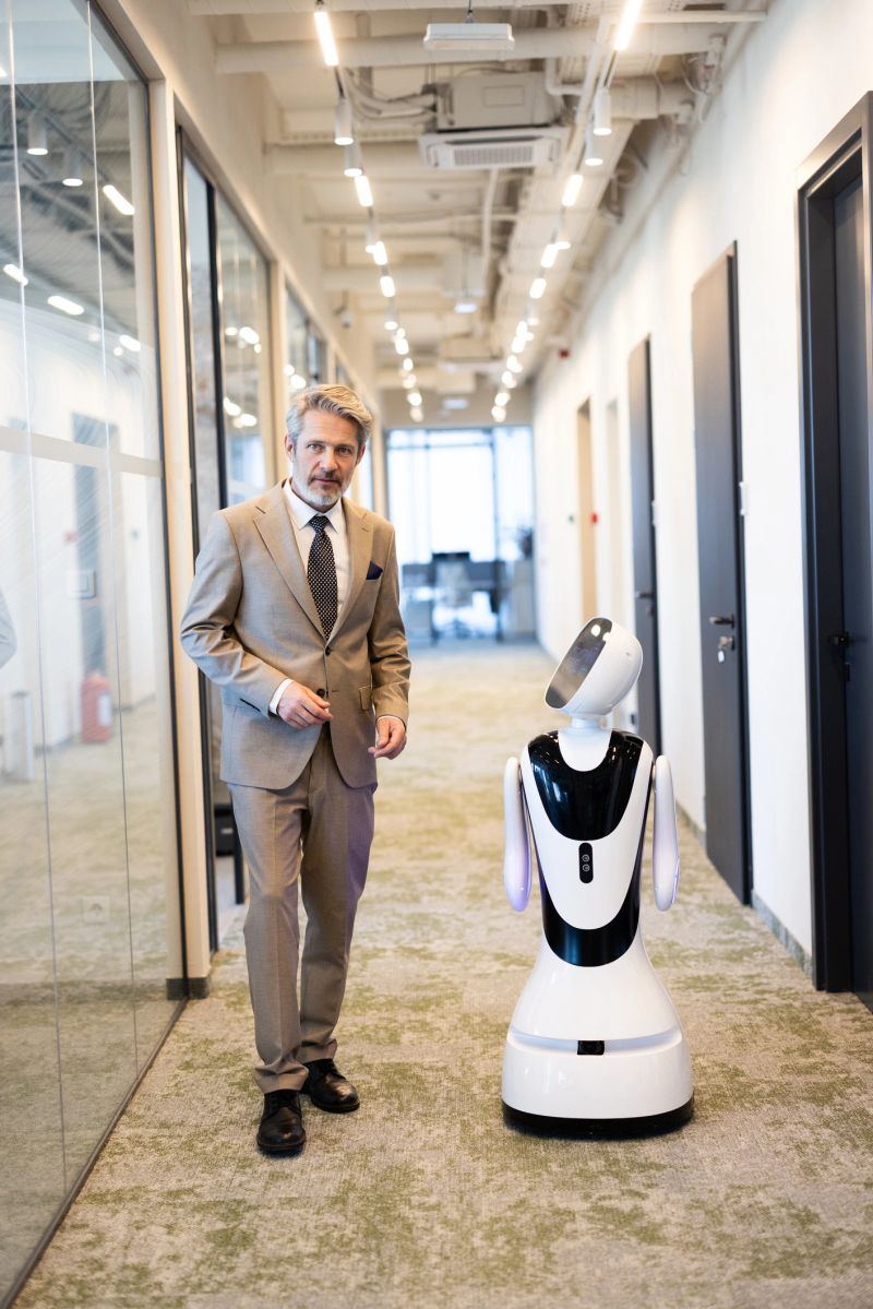 Businessman and service robot walking together through a contemporary corporate office corridor