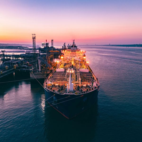 Large cargo ship docked at sunset with industrial structures.