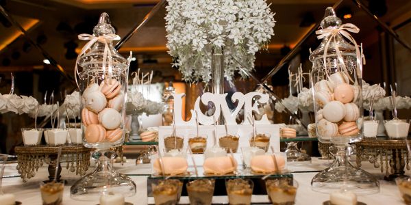 Elegant dessert table with macarons and 'LOVE' sign surrounded by white flowers.