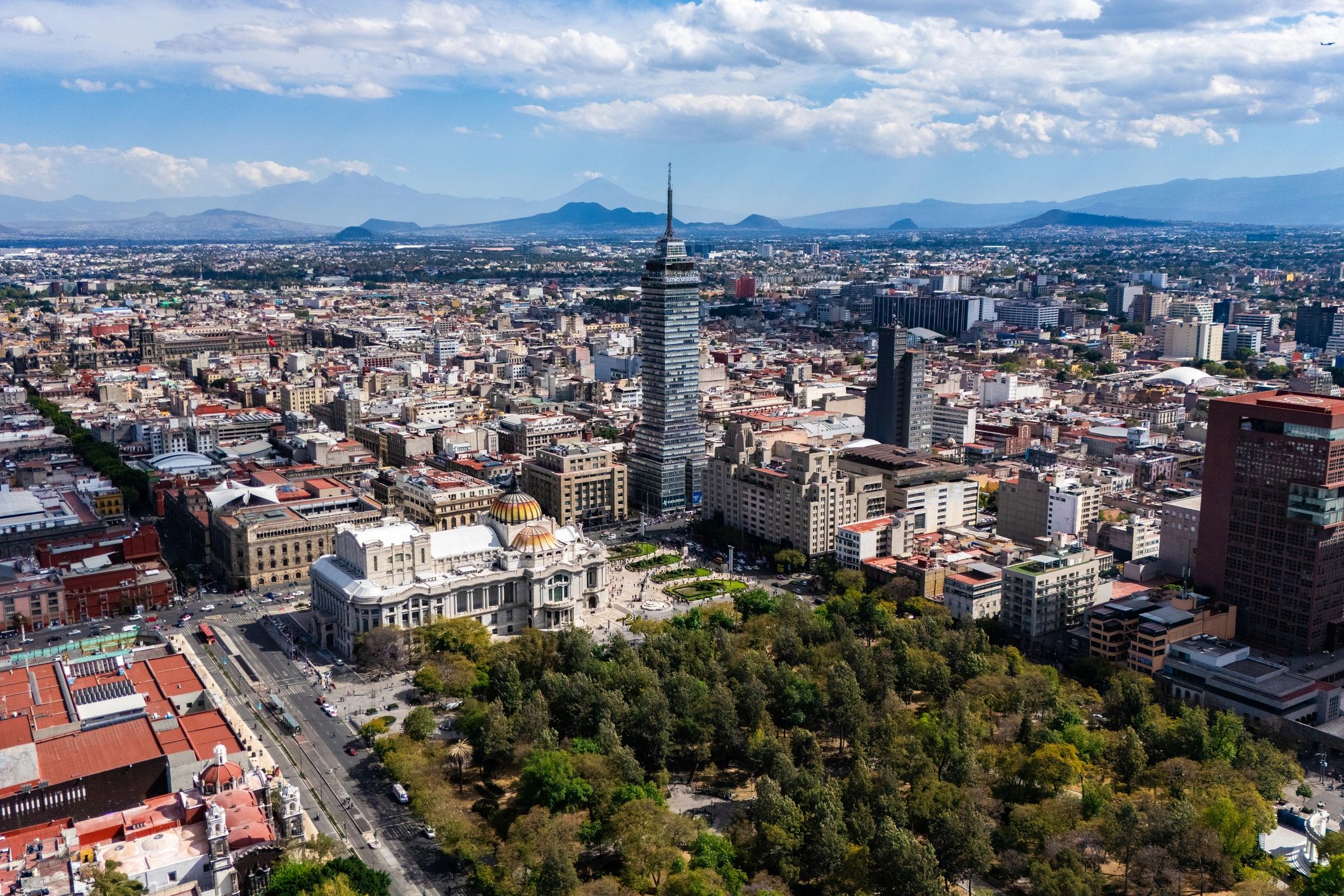 A panoramic cityscape with a tall central tower and distant mountains under a partly cloudy sky.