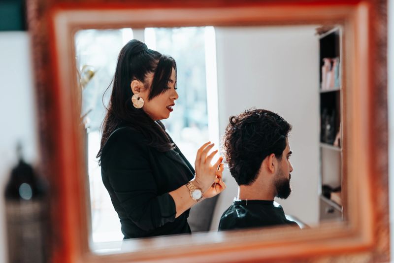 Hair stylist styling a male customer's hair at a modern barber shop, reflecting their interaction and positive experience through a mirror frame, showcasing professional grooming service