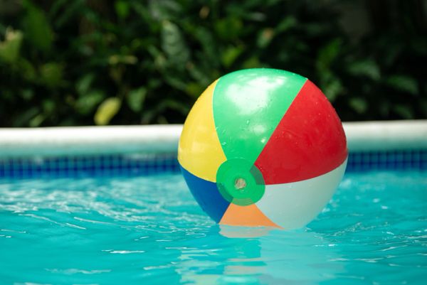 Modern backyard pool with a hot tub and inflatable float, overlooking a serene lake and palm trees.