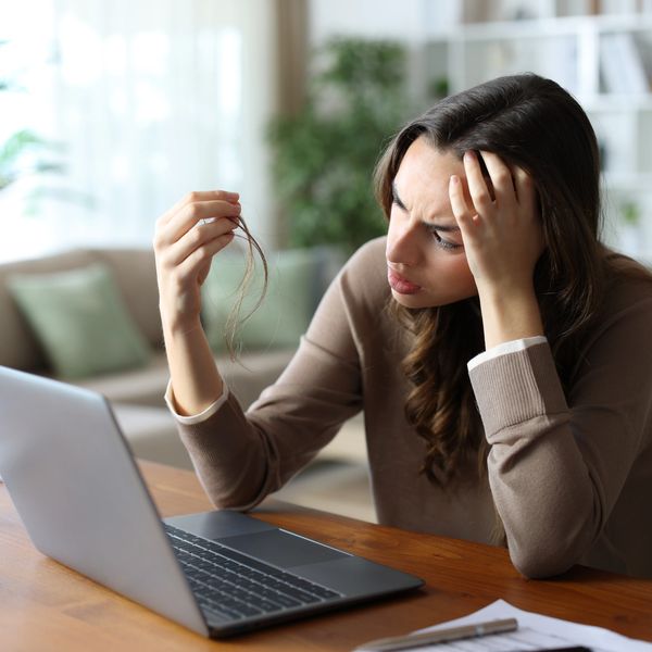 Woman worried about hair loss while working on laptop.