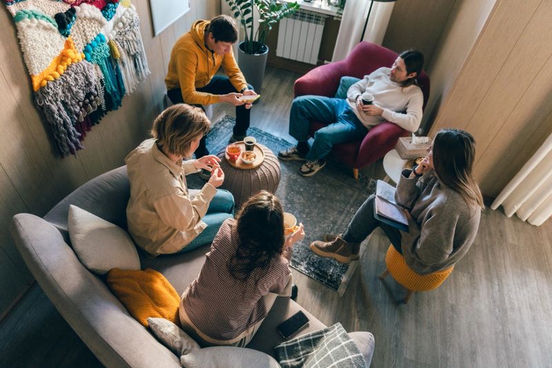 Group of adults sitting together in a cozy living room, drinking coffee and talking, viewed from above, representing social connection and relaxed home lifestyle.