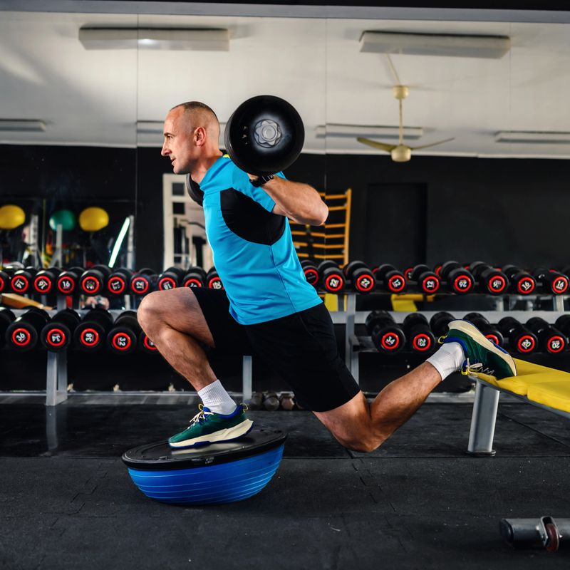 Confident man legs workout with the barbell standing on a balance ball in the gym