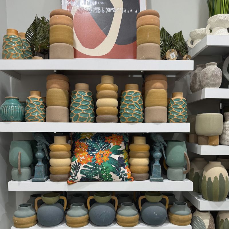 Modern tropical style home decor display with palm tree cushion and ceramic vases on shelves