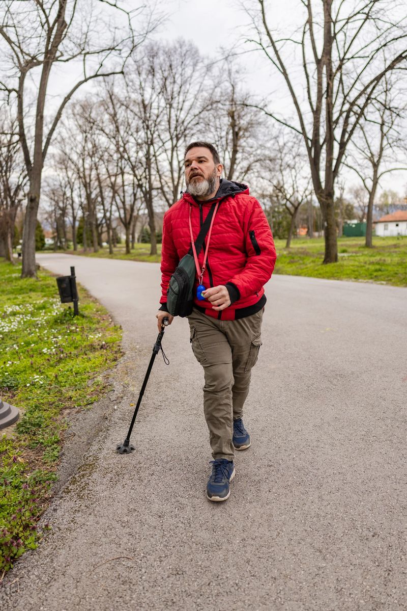 Motivated disabled mature man in red jacket with crutch walking in park