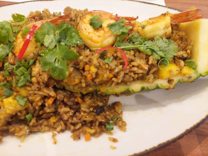 Thai pineapple fried rice, a classic and authentic Thai cuisine, featuring seafood fried rice mixed with sweet pineapple chunks and served inside a hollowed half pineapple. This dish combines savory and fruity flavors, beautifully presented in a natural pineapple bowl, representing vibrant Thai cuisine and tropical street food culture.