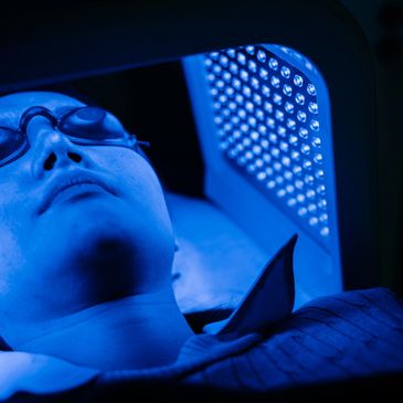 Person wearing protective eyewear under blue light therapy device.