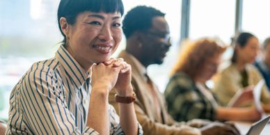Smiling woman in a striped shirt at a meeting with colleagues working in the background.