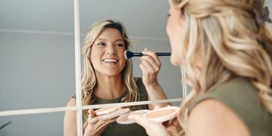 Woman applying makeup in front of a mirror.