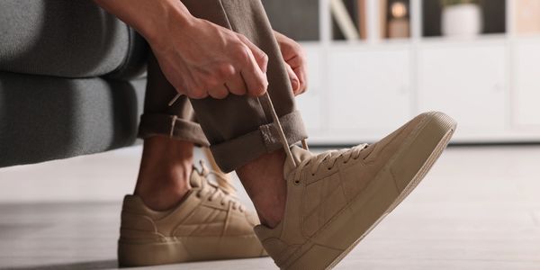 Person tying beige sneakers while sitting on a sofa.