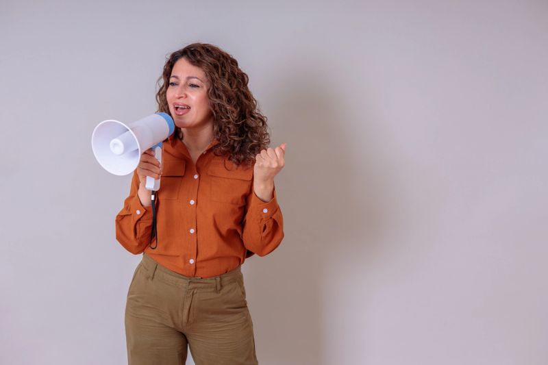 Mature adult woman speaking into a megaphone, making an announcement or leading a protest with conviction and determination