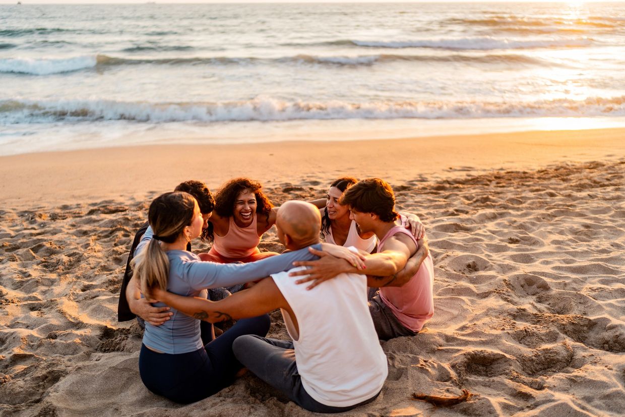 Group of friends sitting in a circle on the beach at sunset.
