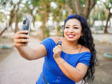 Woman in blue dress taking a selfie outdoors.