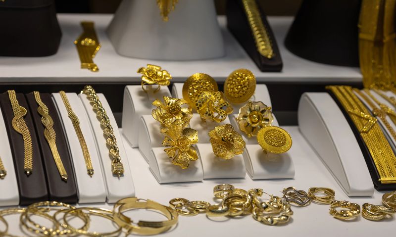 luxury display of ornate 22k gold jewelry featuring intricate filigree flower rings, handcrafted bridal bracelets, and textured bangles in a boutique vitrine.