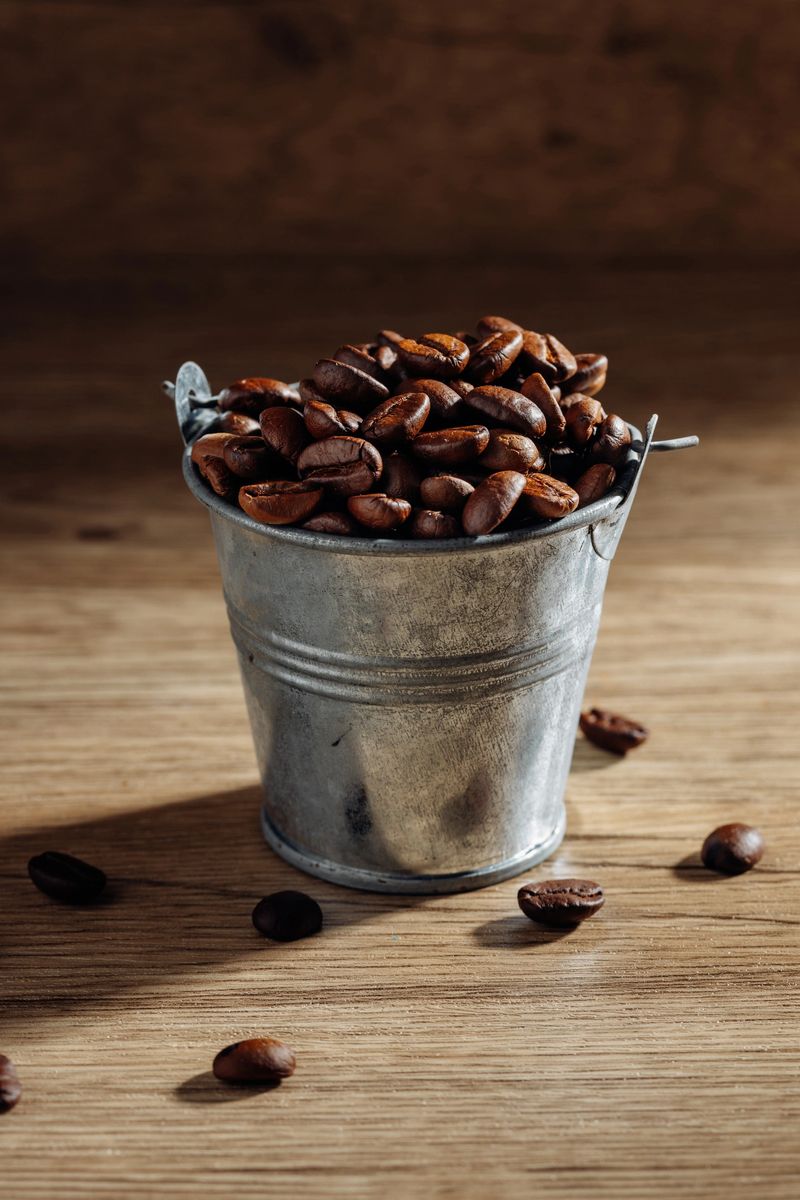 A rustic metal bucket brimming with freshly roasted coffee beans, set against a wooden background. Perfect for coffee lovers and food enthusiasts.