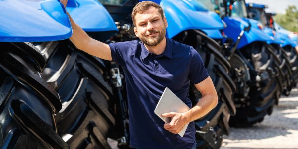 Homem com tablet ao lado de tratores azuis.