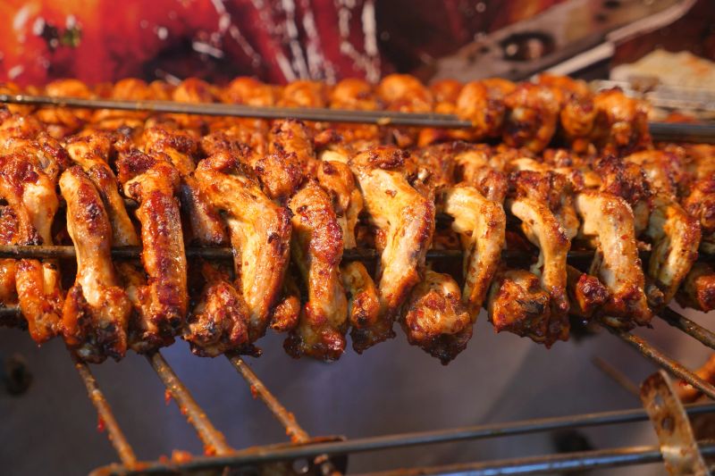 Juicy chicken skewers cooking on a grill in a busy market setting.