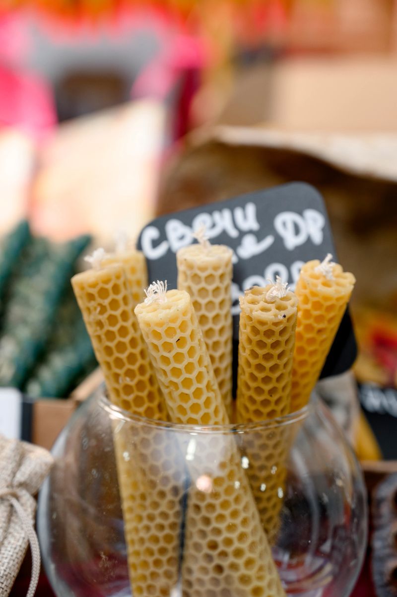 Honeycomb-shaped candles are arranged in a glass jar at a market stall, with a visible price tag and colorful background elements