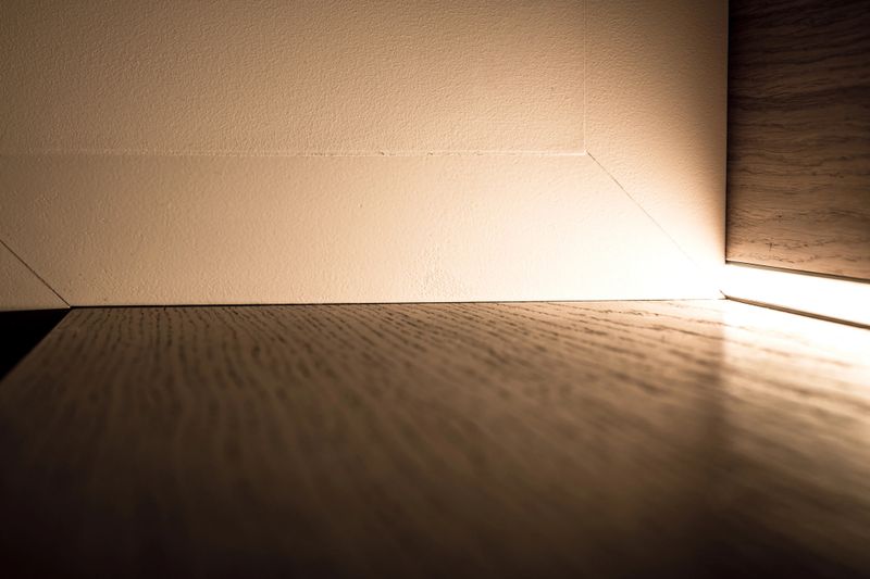 Close-up of a modern wooden stair surface beside a wall with a bright integrated LED light strip along the edge.