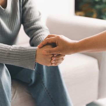 Two people sitting, one comforting the other by holding their hands.