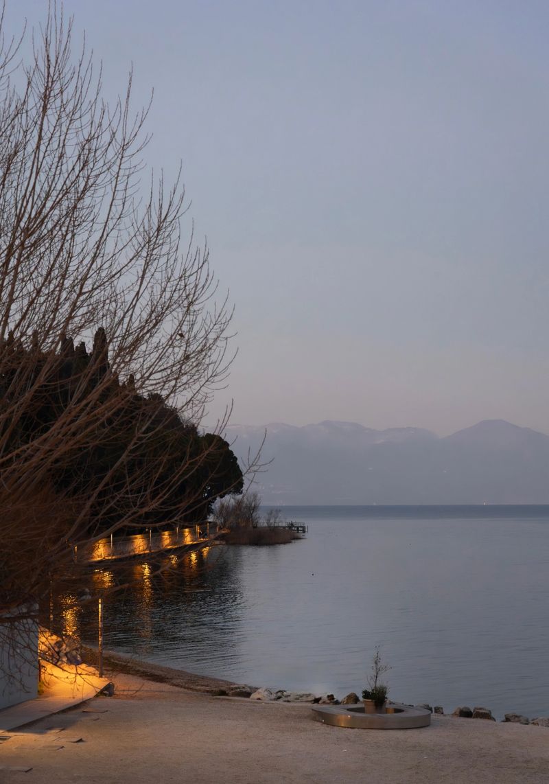 Peaceful evening scene on Lake Garda with illuminated waterfront, calm water and distant mountains. Serene travel landscape in northern Italy.
