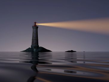 A lighthouse with it's light on shining out over the water.
