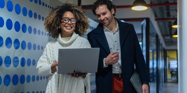 Two colleagues smiling while looking at a laptop.