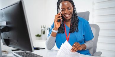 Smiling healthcare worker on phone at desk.