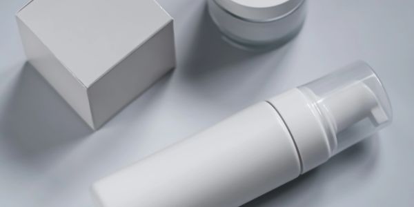 Minimalist white cosmetic containers on a soft grey surface.