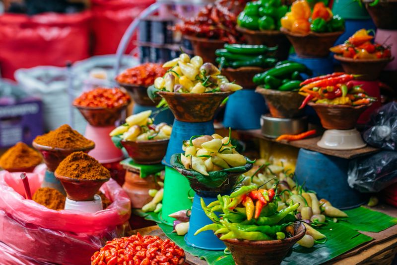 Vibrant market stall in San Cristobal de las Casas, Chiapas, Mexico, displaying assorted chili peppers and ground spices arranged in bowls and baskets, conveying local flavor, culture, and lively street market atmosphere.