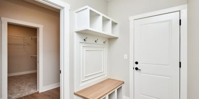 Entryway with a white door, wooden bench, and coat hooks.