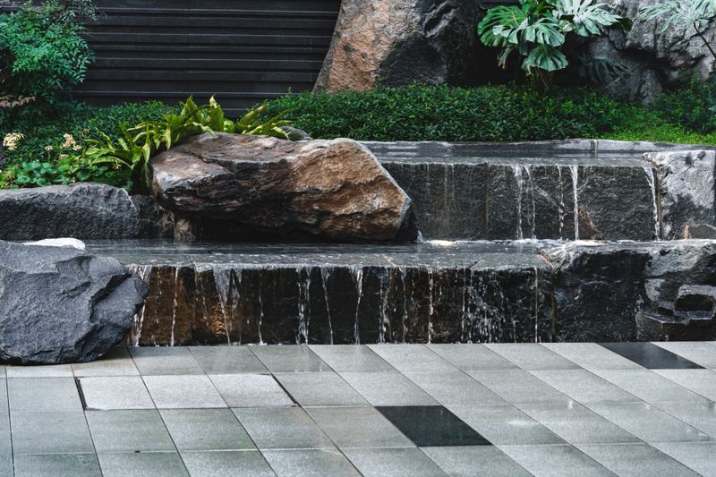 Tiered stone water feature with gentle cascades flows into a shallow pool. Scene details: calm, serene, contemporary