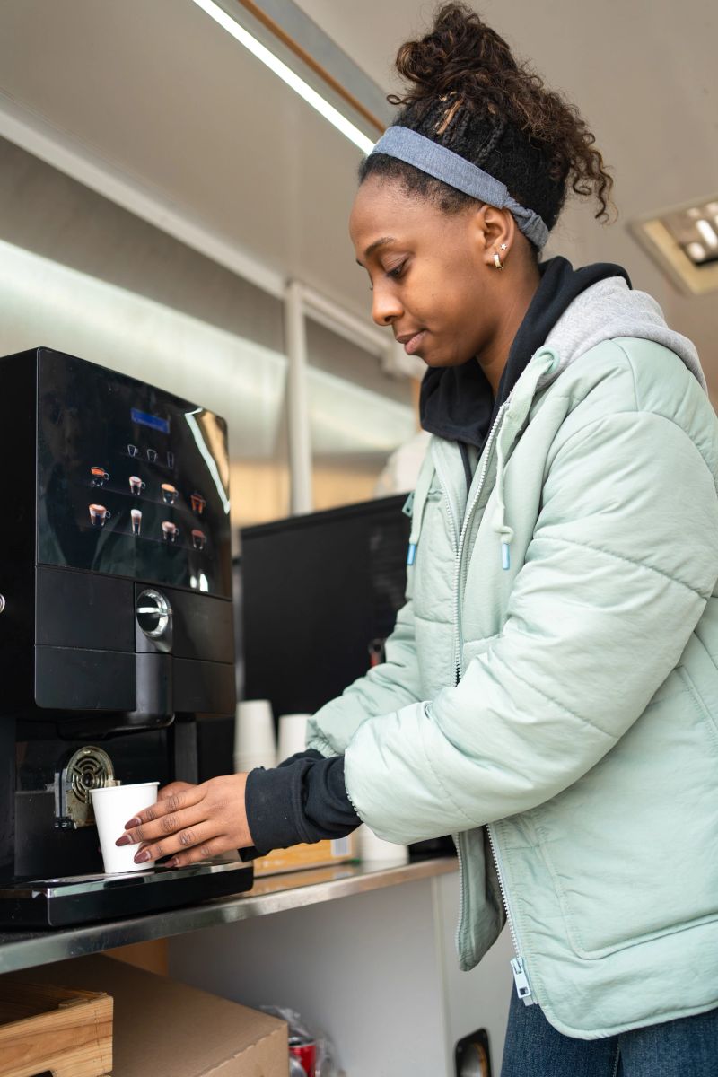Woman standing at a counter making hot coffee using an automatic machine