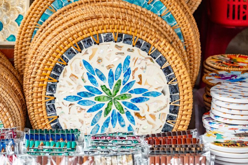 This is a handmade Vietnamese rattan tray with a decorative mother-of-pearl (shell) mosaic center. The outer frame is woven from bamboo or rattan, while the central design is created by embedding polished shell pieces into resin. These trays are commonly sold in markets across Vietnam as both functional serving trays and decorative items, often used for home décor or wall display.