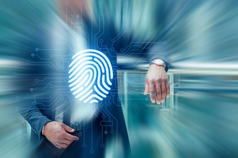 A businessman stands confidently with one hand on a railing in an office space. A digital fingerprint symbol appears in the foreground, indicating security or identification.
