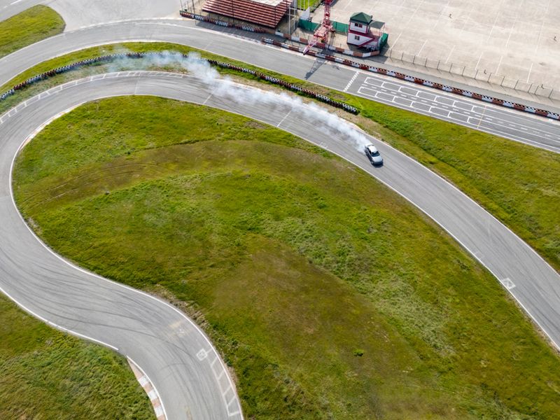 Car performing drift maneuver on asphalt race track, generating smoke from tires