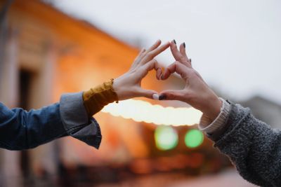Two hands forming a heart shape with blurred lights in the background.