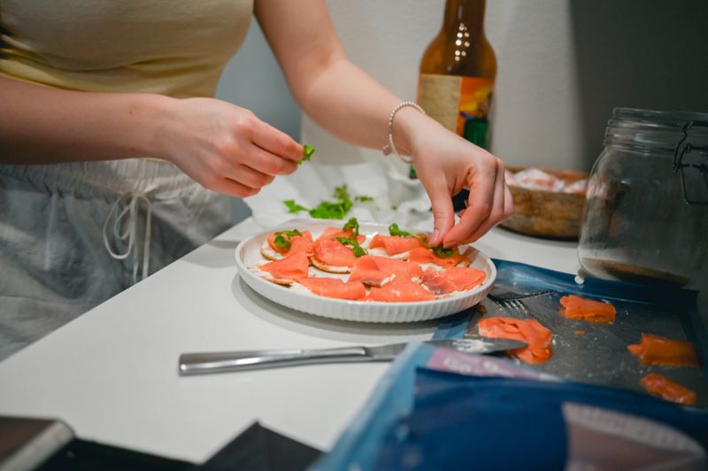 Woman preparing smoked salmon snacks with cream cheese and fresh herbs in a kitchen