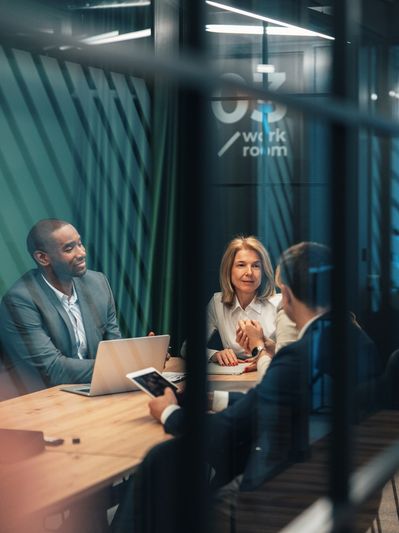 Three professionals in a meeting room discussing work.