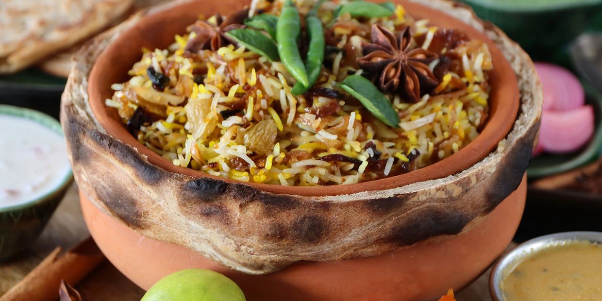 Traditional biryani served in a clay pot with spices and green chili garnish.