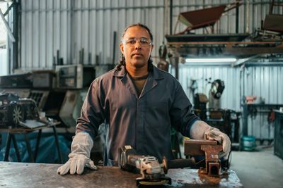 A worker in protective gloves stands in a workshop with tools on the table.