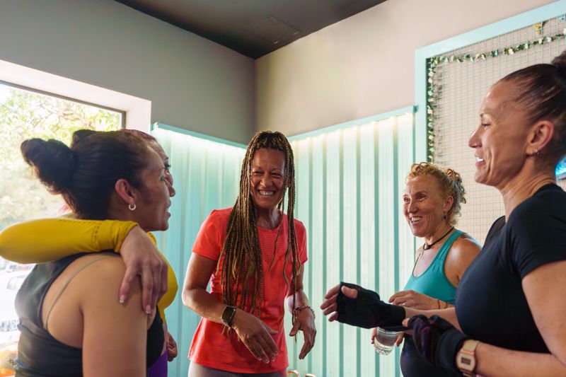 Group of diverse mature adult women enjoying a conversation and laughing together during a fitness workout break at the gym