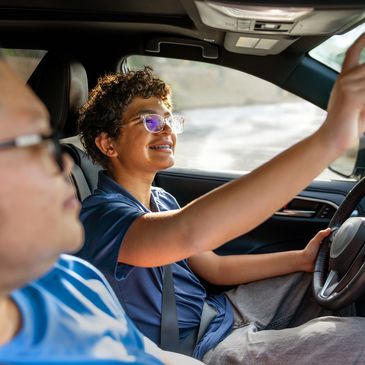 Young man driving car, smiling, adjusting rearview mirror.