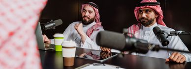 Men in traditional attire recording a podcast with microphones and coffee cups.